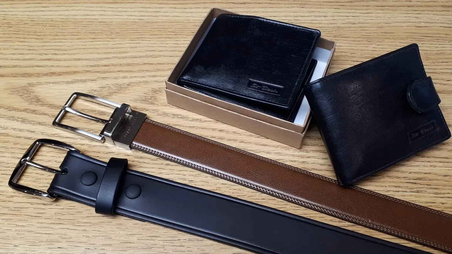 Deux ceintures de cuir, un portefeuille noir en boîte et un porte-cartes, posés sur le comptoir de bois.