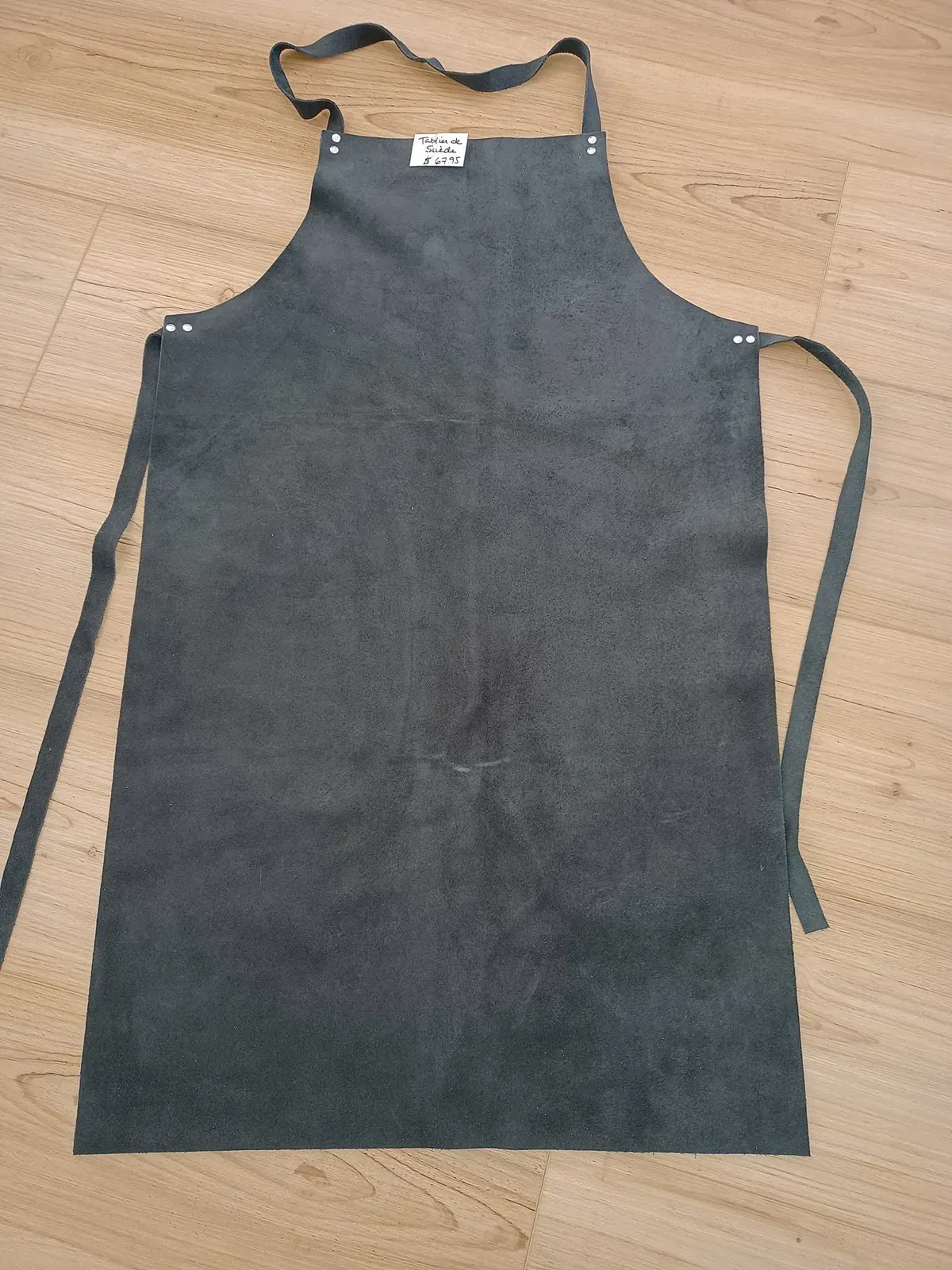Tablier de suède gris foncé étendu, avec une étiquette de prix écrite à la main.