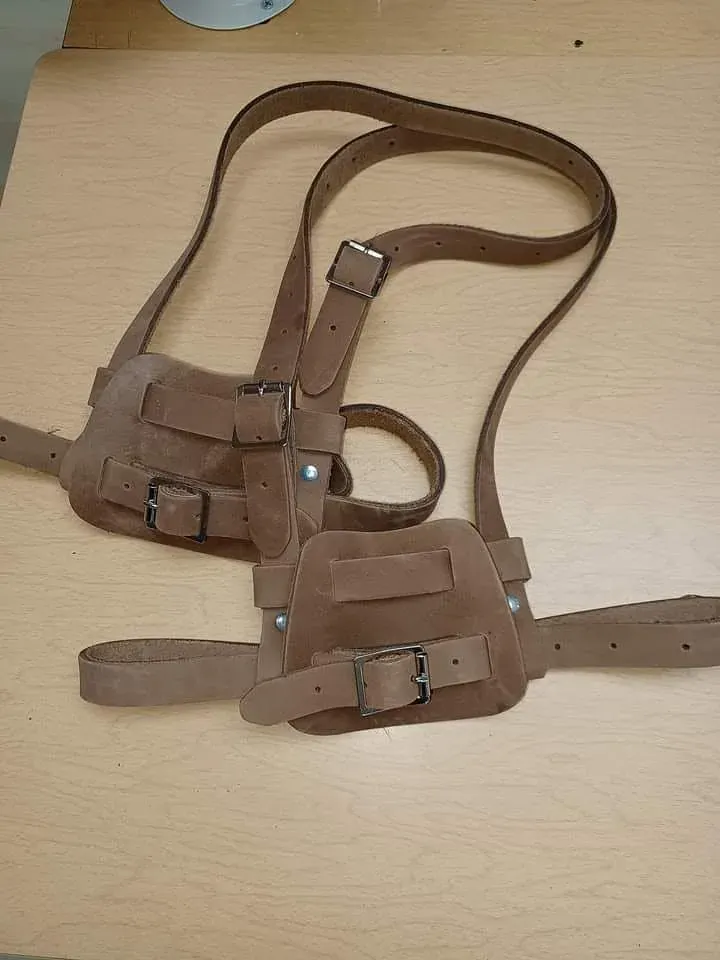 Porte-outils de cuir brun vu de haut, bretelles déployées sur l’établi.