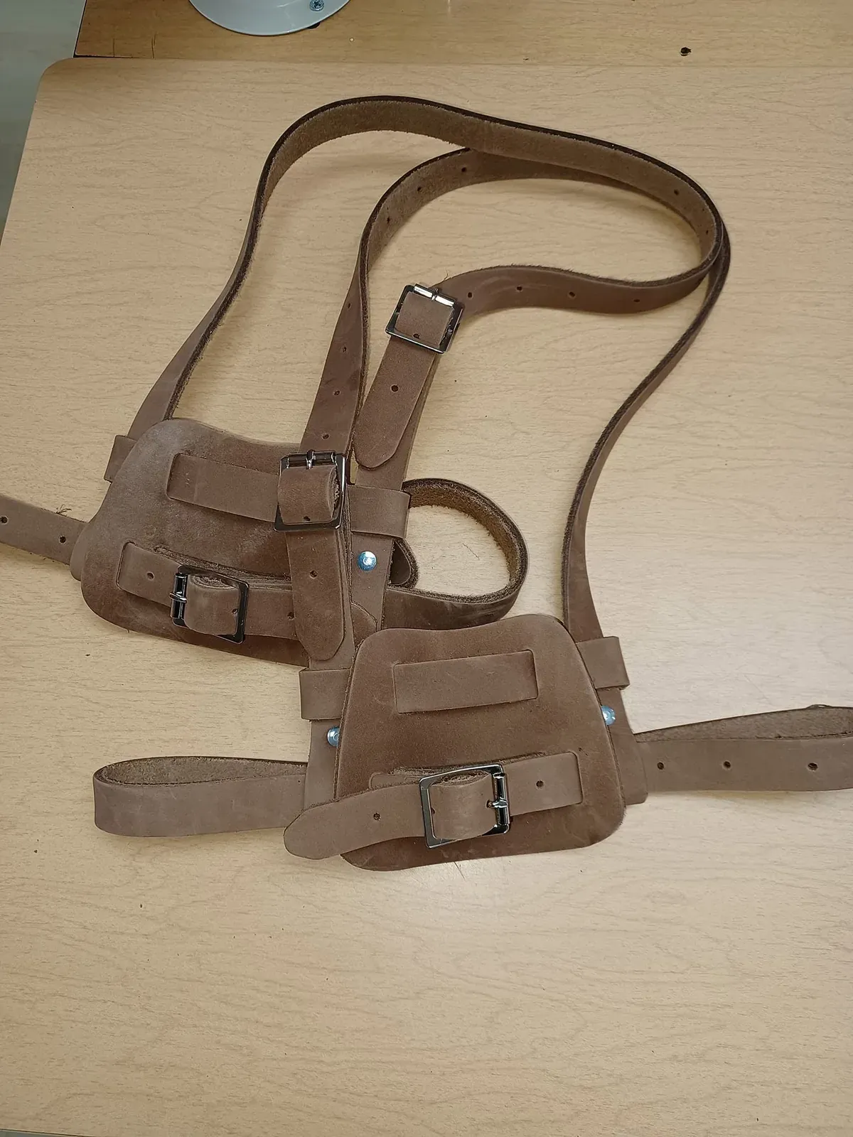 Porte-outils de cuir brun à bretelles et boucles, posé sur l’établi.