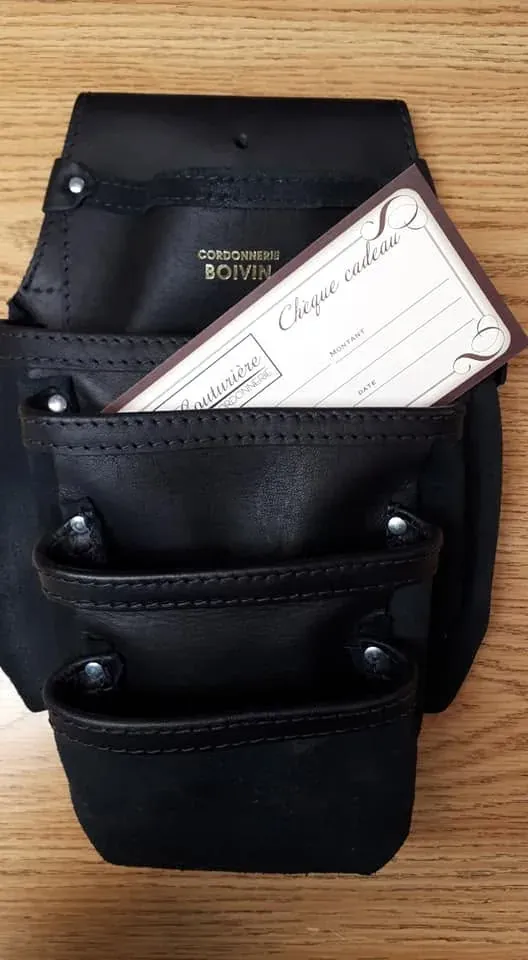 Sac à outils en cuir noir marqué Cordonnerie Boivin, un chèque-cadeau dépassant de la poche.