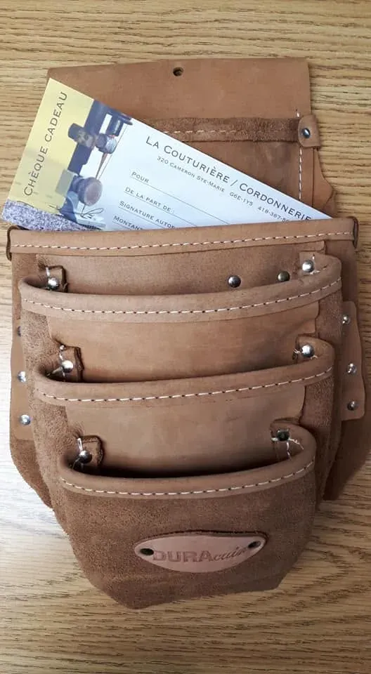 Sac à outils en cuir suédé brun à trois poches, avec un chèque-cadeau au nom de La Couturière / Cordonnerie glissé dans la poche arrière.