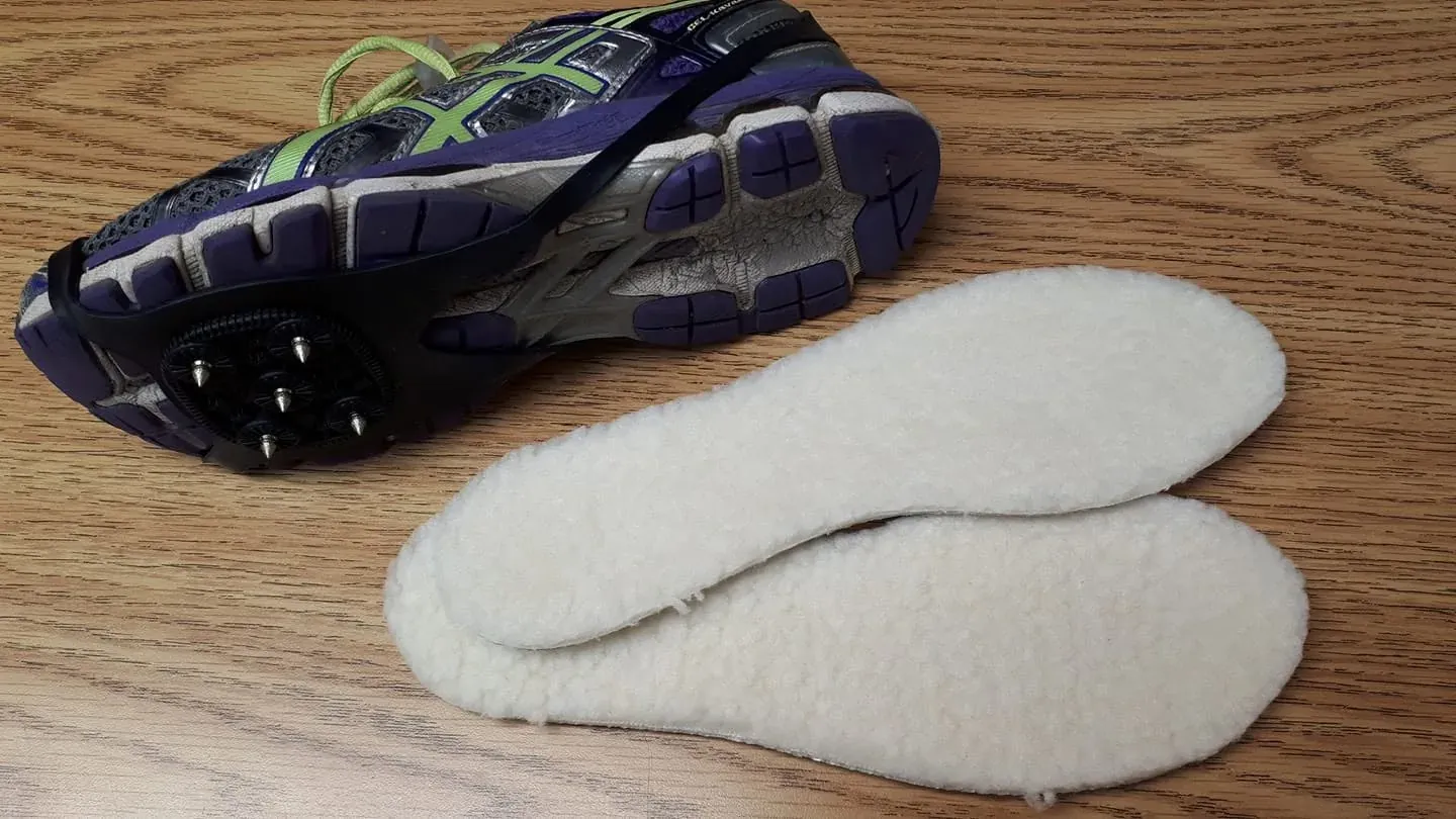 Chaussure de course retournée montrant des crampons fixés sous la semelle, à côté de deux doublures de mouton blanches, sur le comptoir de bois.